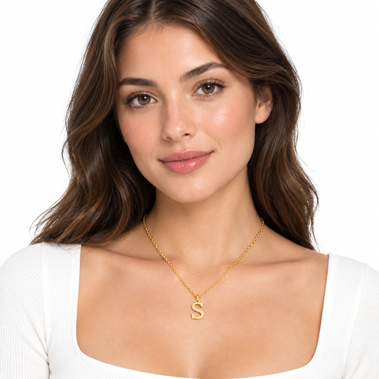 Modelka w złotym naszyjniku z literą S, na białym tle