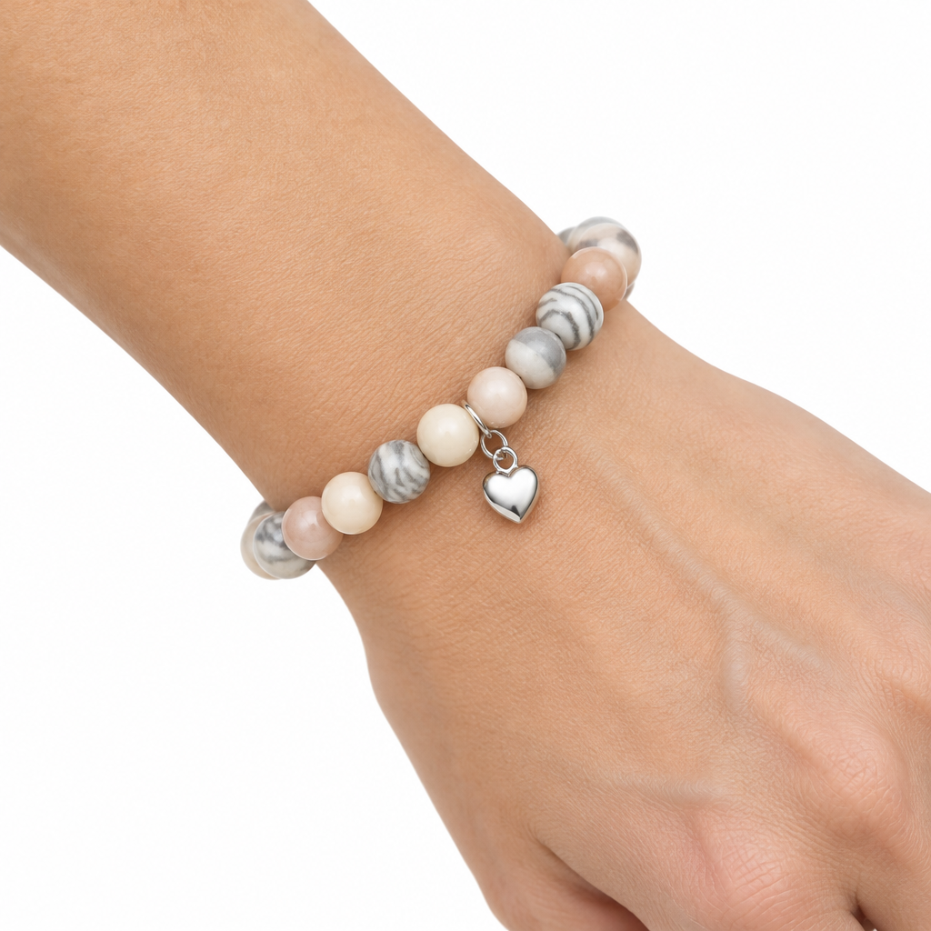 Bransoletka z jasnymi koralikami i serduszkiem na nadgarstku modelki, biale tlo