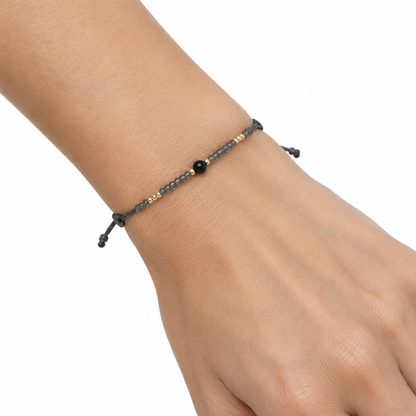 Ciemna bransoletka boho z czarnym koralikiem na nadgarstku modelki, biale tlo